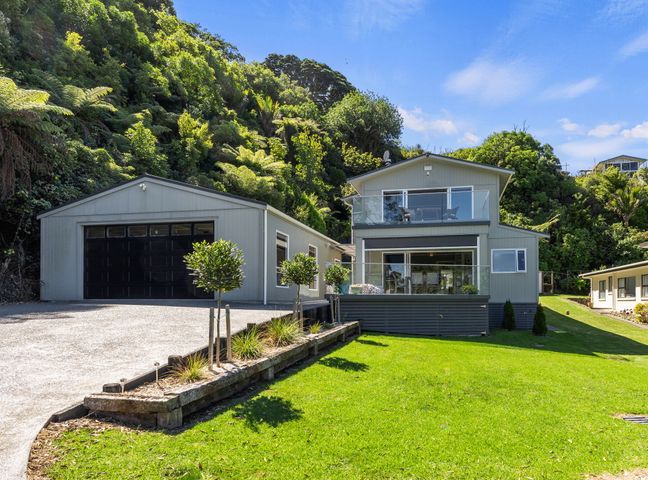 A two-story house with a garage and balcony surrounded by trees and lawn at The Lighthouse - Te Mata Holiday Home in Te Mata