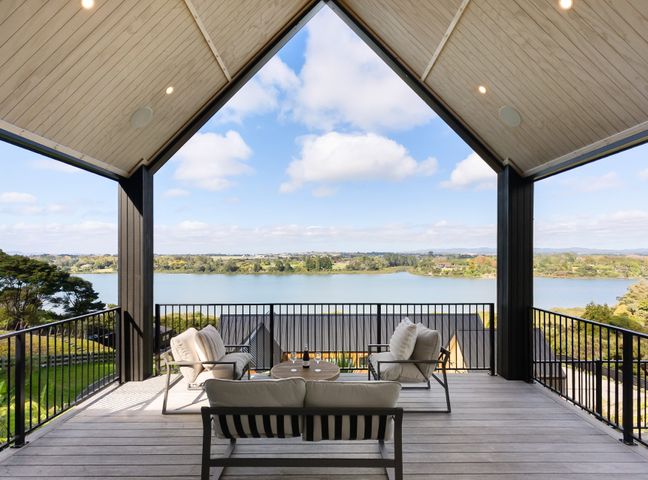 A balcony with cushioned chairs and a small table overlooking a body of water at Estuary Views - Riverhead Holiday House in Riverhead
