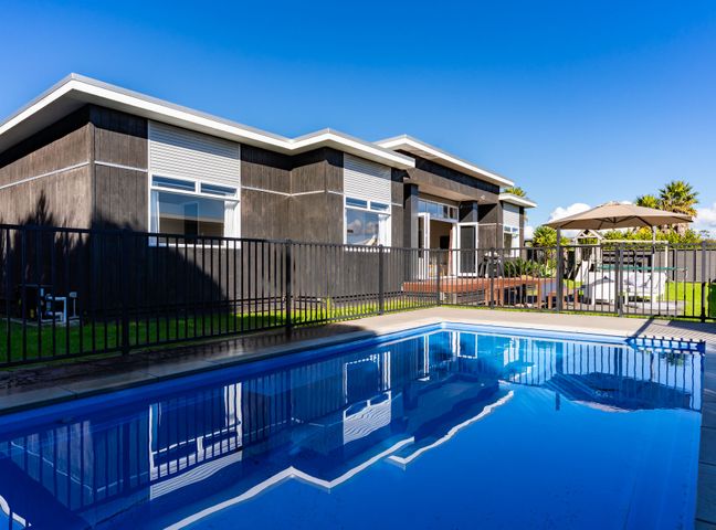 An outdoor area with a swimming pool and a house at Mangawhai Heads Holiday Home in Mangawhai