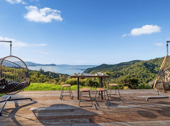 A dining area with hanging chairs and a view of the ocean at Little Tui Ridge - Coromandel Holiday Home Coromandel
