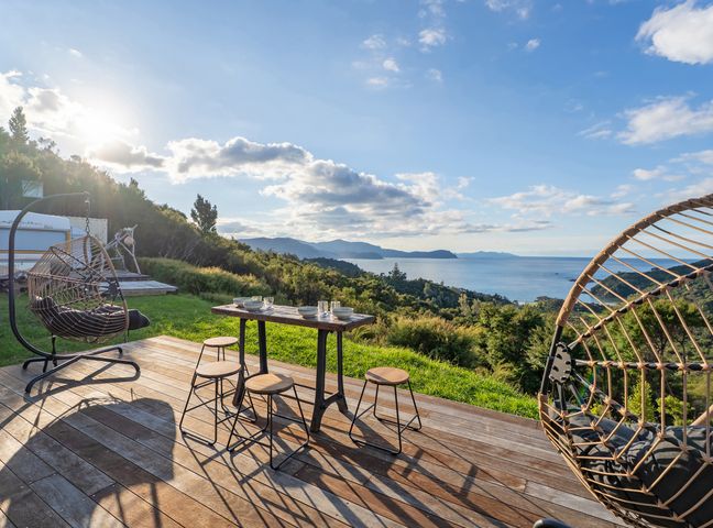 An outdoor area with a table and chairs overlooking the ocean at Little Tui Ridge - Coromandel