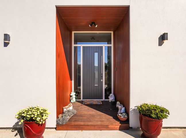 An entryway with a front door and flower pots at Ohana - Papamoa Holiday Home