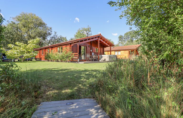 A wooden cabin with a covered patio and outdoor seating surrounded by grass and trees at Jemima Lodge in Tattershall