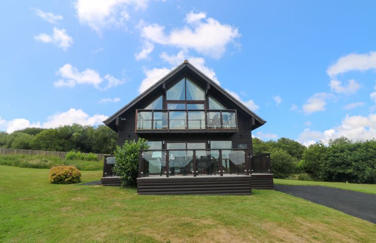A two-story wooden lodge with glass balconies on a grassy lawn at Willow Retallack in Retallack near St Columb Major