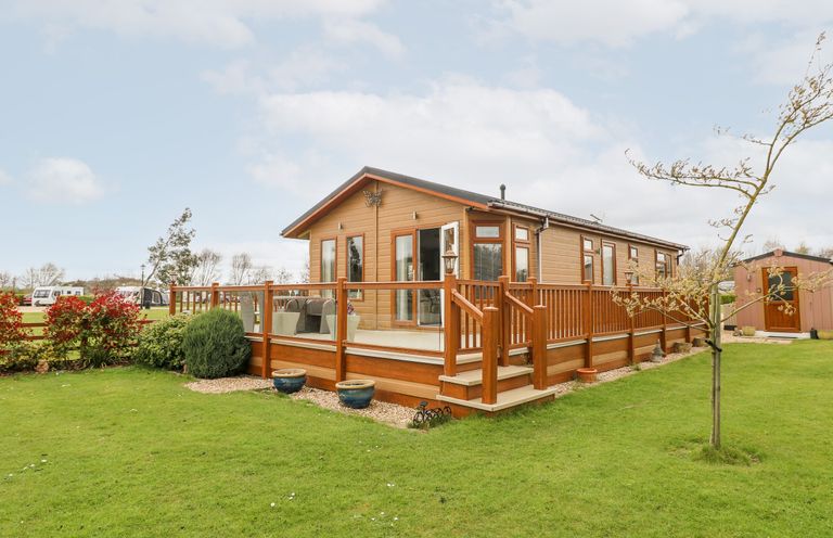 A wooden lodge with glass-paneled deck and outdoor seating on a grassy lawn at Lake View Lodge in Marston near Barkston