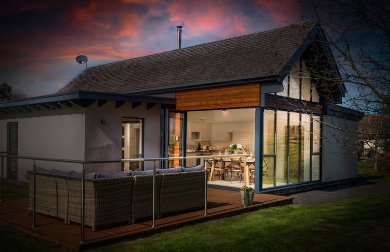 A house with an outdoor seating area and a kitchen visible through large glass doors at Lambs Lodge in Bamburgh