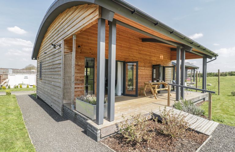 A wooden cabin with a covered porch and picnic table in a grassy area at Primrose Sticklinch West Pennard Glastonbury