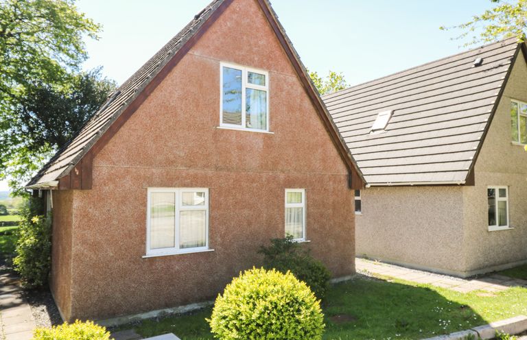 Two houses with triangular roofs and windows surrounded by grass and bushes at Dartmoor 2 in Callington