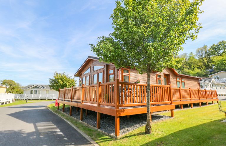A wooden cabin with a wraparound deck and a tree in front at Serendipity - Heritage Park Stepaside near Kilgetty