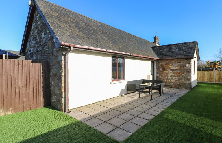 An outdoor patio area with tiled floor artificial grass seating and stone and white walls at The Old Well Bungalow - Ty Mawr Farm in Cardiff