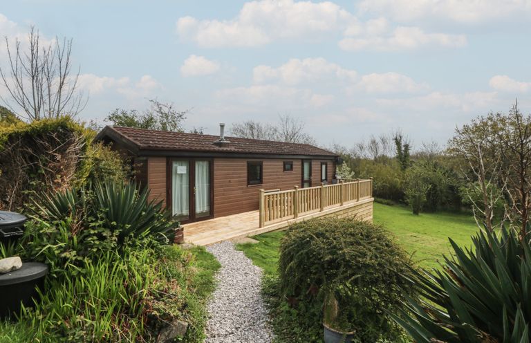 A wooden cabin with a deck and gravel path at Castell Chalet in Penrhos near Pwllheli