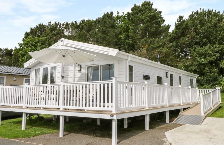 A white mobile home with a wraparound deck and umbrella surrounded by trees at Cayton Pines in Cayton Bay near Scarborough