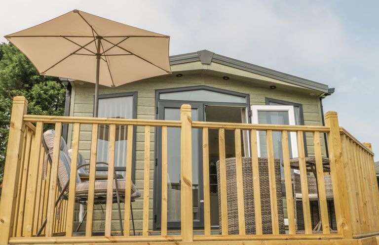 A wooden deck with outdoor chairs umbrella and table outside a small building at The Sequoia in Cloughton