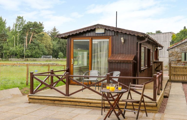 A wooden cabin with glass door and outdoor seating area with table and chairs at Thirley Beck Lodge in Harwood Dale