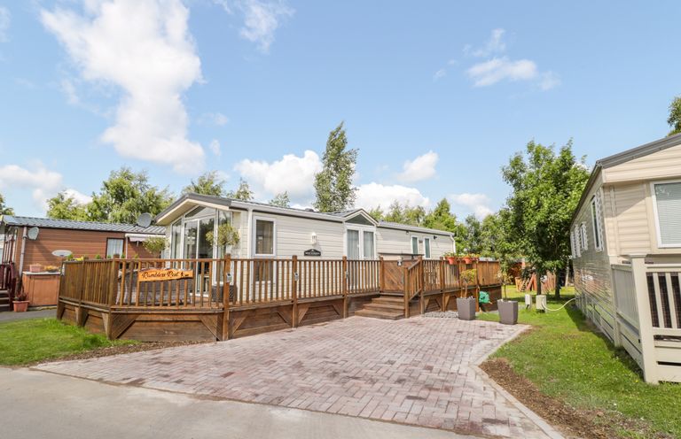 A residential park home with a wooden deck and paved driveway surrounded by trees at Ramblers Rest in Felton