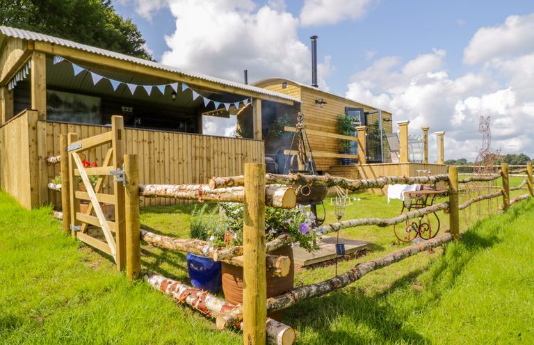 A wooden cabin with a fenced garden and a seating area at High Rigg Shepherd's Retreat in Brampton Cumbria