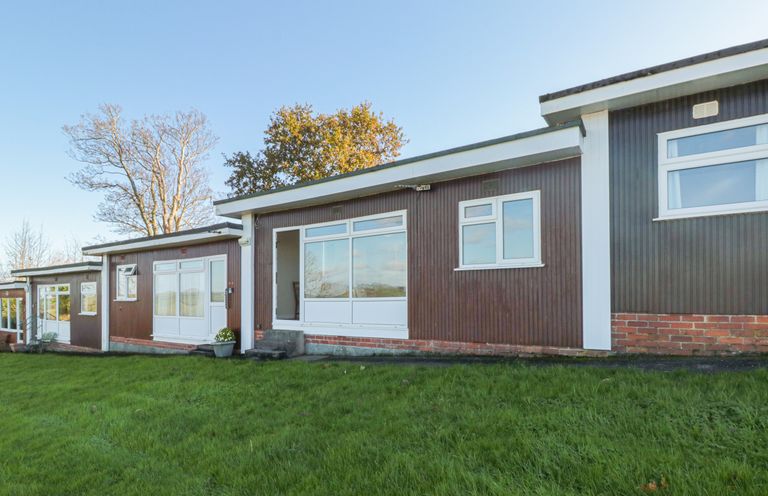 A view of a brown exterior wall with white framed windows and doors on a building with grassy lawn in front at 304 Norton Park in Dartmouth