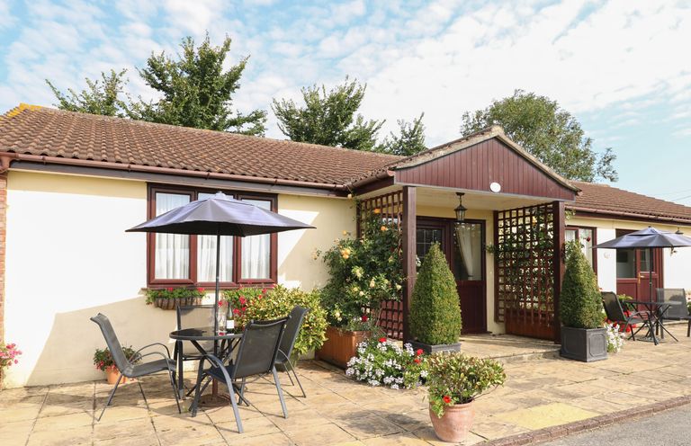 An outdoor patio area with tables umbrellas chairs and potted plants in front of a single story building at Willow Barn in Cucklington near Wincanton