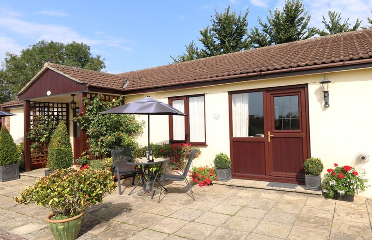 An outdoor patio area with a table umbrella and chairs in front of a building with brown doors and windows at Little Barn in Cucklington near Wincanton