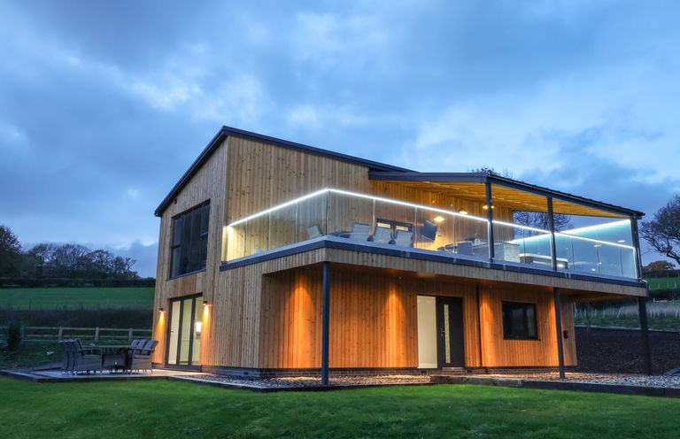 A modern two-story wooden house with an upper balcony and outdoor seating on a lawn at Fron Haul - Robin Goch in Llanfwrog near Ruthin