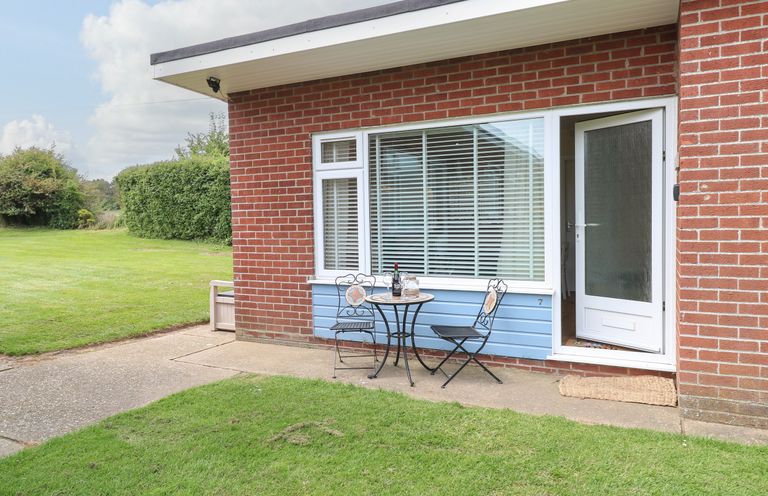 A small outdoor patio with a round table and two chairs outside a brick building with a white door and large window at The Cranny in Mundesley