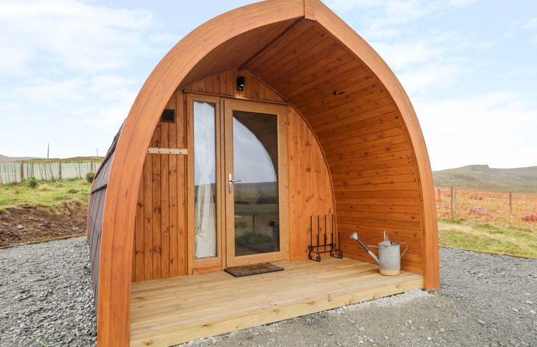 A wooden pod structure with a glass door and small porch area with a watering can at Garraidh Ghorm Pod in Conista