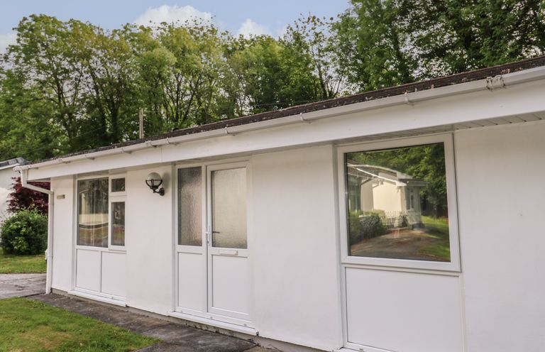 The exterior of a white single-story building with multiple windows and a door surrounded by trees at 11 Tremore in Liskeard