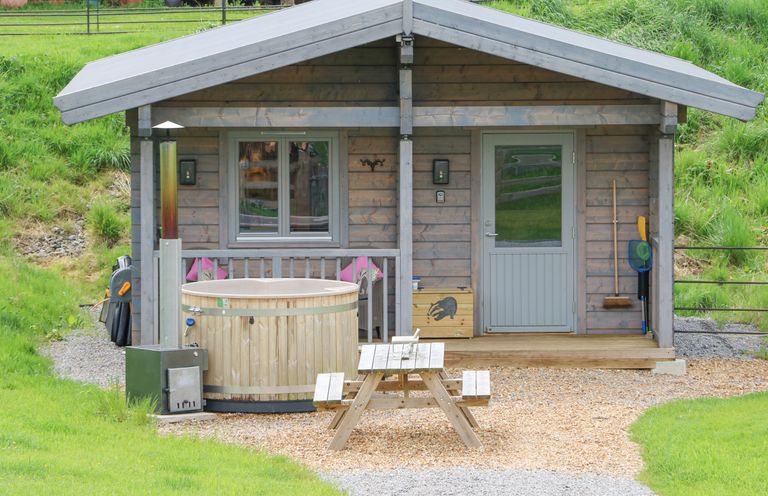 A small wooden cabin with a hot tub picnic table broom and net outside at Badgers Sett Winston near Staindrop