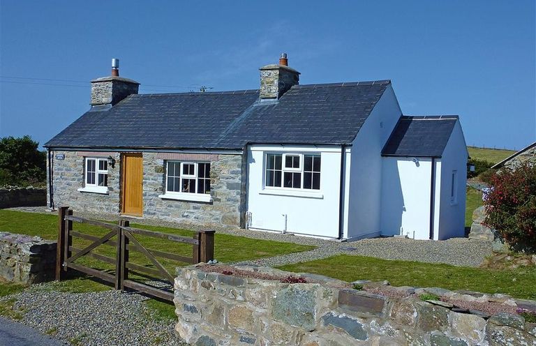 A stone and white cottage with a wooden gate and low stone wall at Gwndwn Gwyn in Trefasser Near Strumble Head