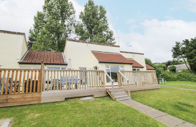 A bungalow with a wooden deck and outdoor furniture on a grassy lawn at 9 Manorcombe Bungalows in St Ann's Chapel near Callington