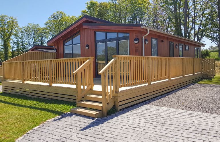 A wooden cabin with large windows and a surrounding wooden deck with railing at Wren Lodge in Gargrave