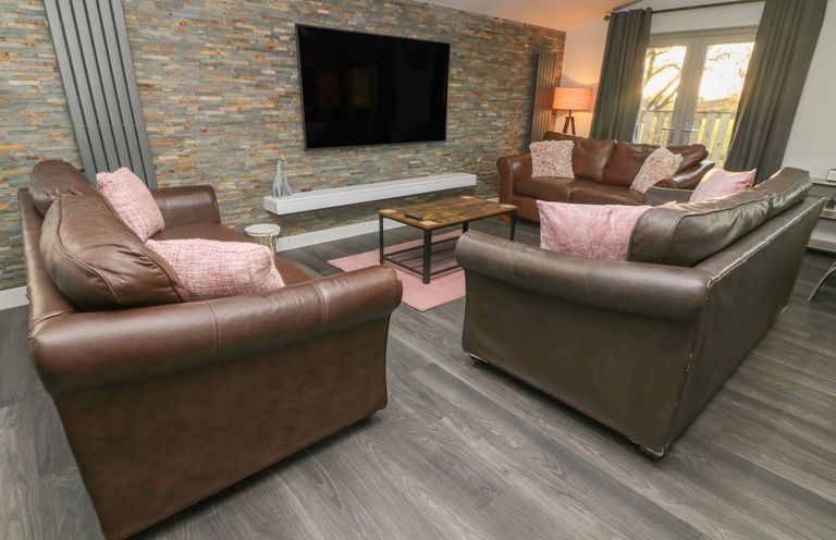 A living room with three brown leather sofas a wall-mounted flat screen television and a coffee table at Box Tree Escapes Wennington near Kirkby Lonsdale