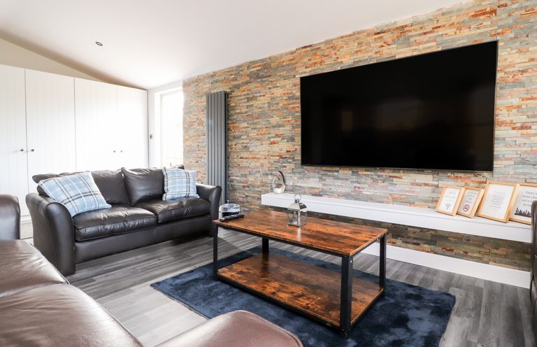 A living room with leather sofas a wooden coffee table and a large wall mounted television at Box Tree Escapes Wennington near Kirkby Lonsdale