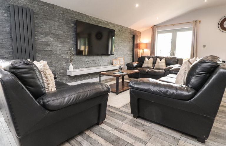 A living room with black leather sofas a wooden coffee table a wall-mounted flat screen television and a stone accent wall at Box Tree Escapes in Wennington near Kirkby Lonsdale
