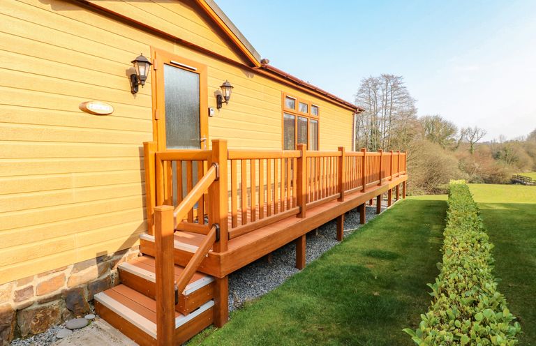 A wooden house exterior with stairs and a railing leading to a door and a lawn with a hedge at Jules @ 79 in Stepaside