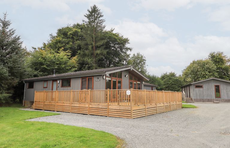 A wooden lodge with a deck and trees at The Loghey in Hawkshead