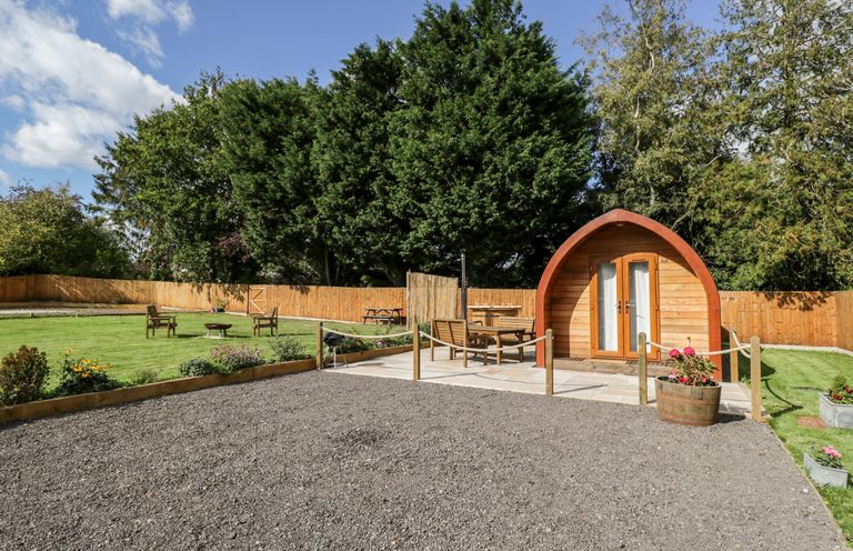 A garden area with a wooden pod seating and chairs on patio with trees and fence at Halmore Pod Halmore near Berkeley