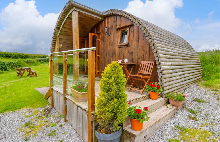 A wooden cabin with glass railing and potted plants on a porch in a grassy area at Oak View in Llandovery