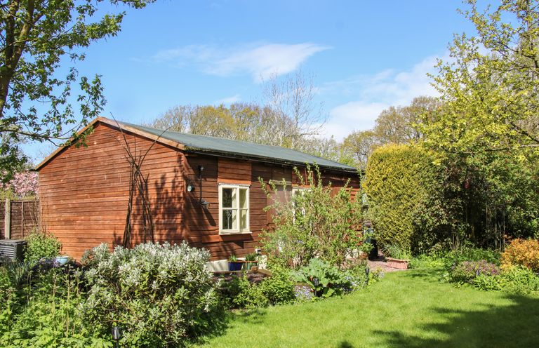 A garden with bushes grass and trees beside a wooden shed at The Garden Lodge in Upton Cressett near Bridgnorth