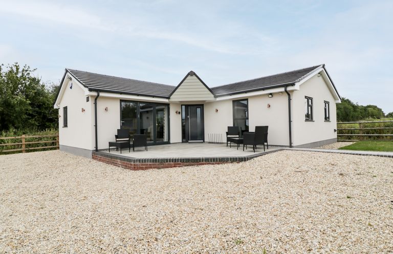 A single story white house with gray roof and patio furniture on a gravel yard at Strawberry Stables in Iwood near Congresbury