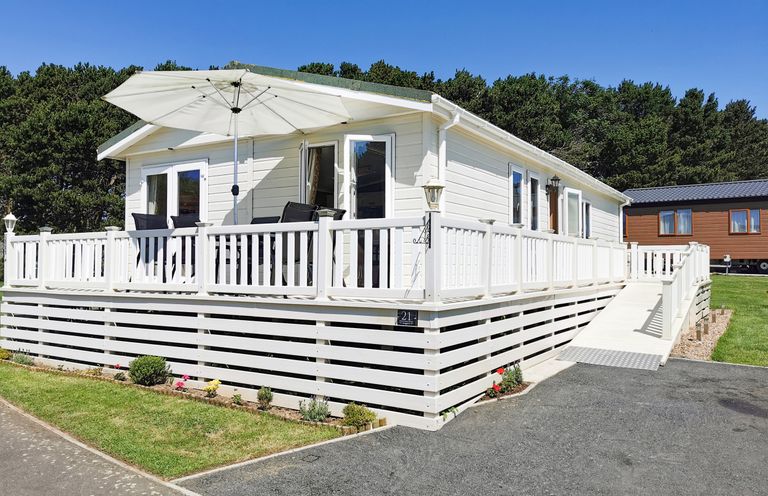 A white mobile home with a deck and outdoor furniture under an umbrella at Jonstone Pines in Cayton Bay near Scarborough
