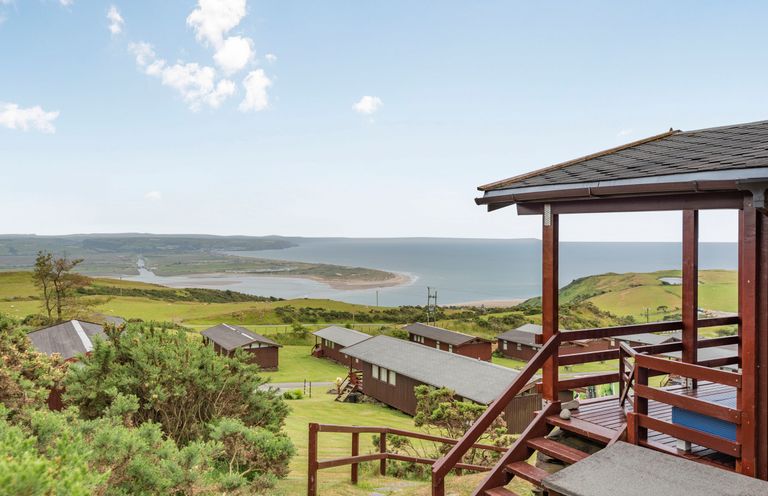 A coastal view with cabins and grassy hills and a covered wooden deck at The Look Out in Aberdovey