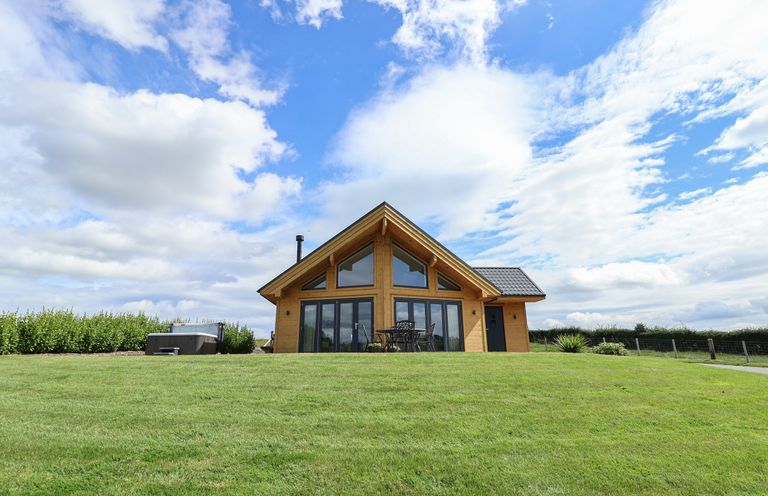 A wooden house with large glass windows a table with chairs and a hot tub on a grassy lawn at Pen Bryn in Cyffylliog near Ruthin