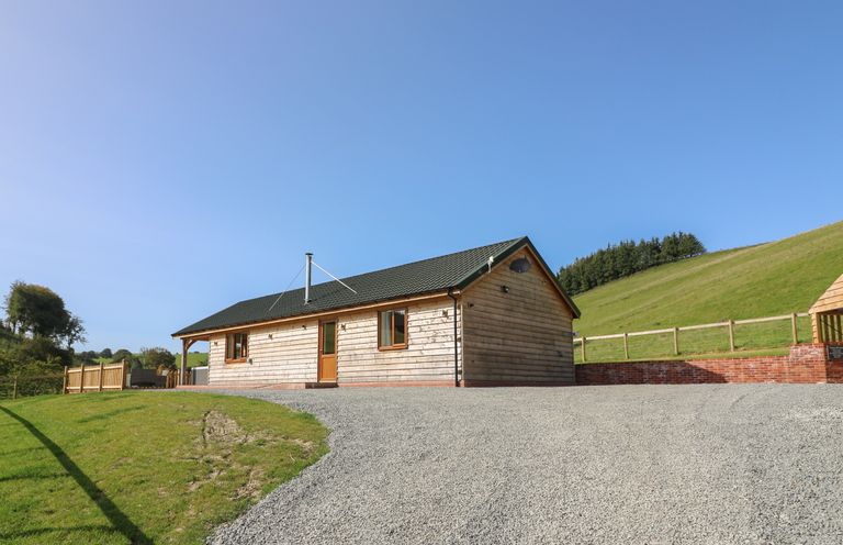 A wooden cabin with a gravel driveway and grass on a hillside at Ploony Hill Cabin in Bleddfa near Knighton