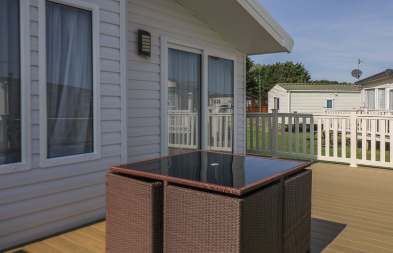 An outdoor deck area with a glass top table and wicker chairs outside a house at Daisy Lodge in Cayton Bay near Cayton