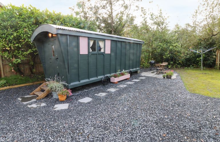 A garden area with a small green caravan a gravel path and outdoor seating at Hazel Nook in Narberth