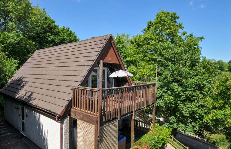 A two-story house with a sloped roof and wooden balcony surrounded by trees at 59 Valley Lodge Callington near Gunnislake