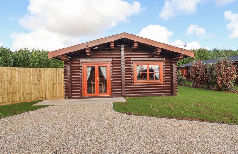 A front view of a wooden log cabin with gravel driveway and a small grass lawn at Maple Lodge in Greetham Rutland