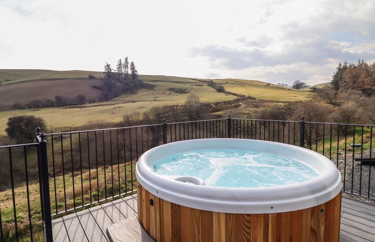 A hot tub on a deck overlooking fields and hills at The Sheep Shed in Llanrhaeadr-Ym-Mochnant