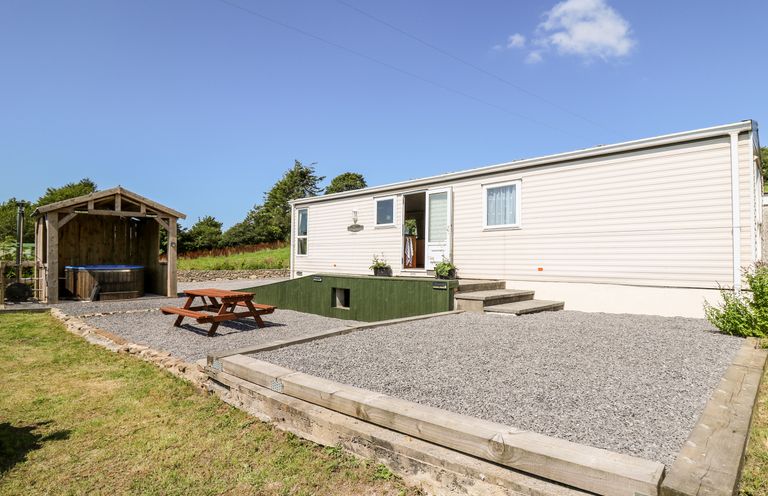 An exterior view of a mobile home with gravel patio area wooden picnic table and covered hot tub at The Lodge in Pontyates